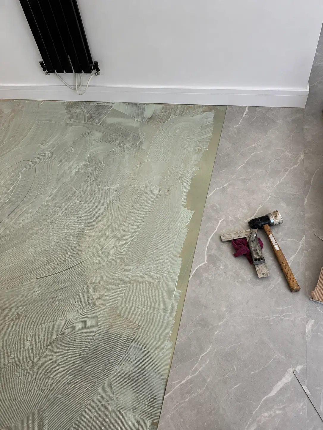 Adhesive combed across a prepared subfloor beside marble tiling and fitting tools on a Pristine Flooring project
