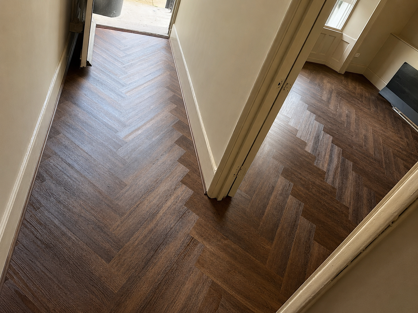 Dark brown herringbone flooring flowing through a hallway and adjoining rooms