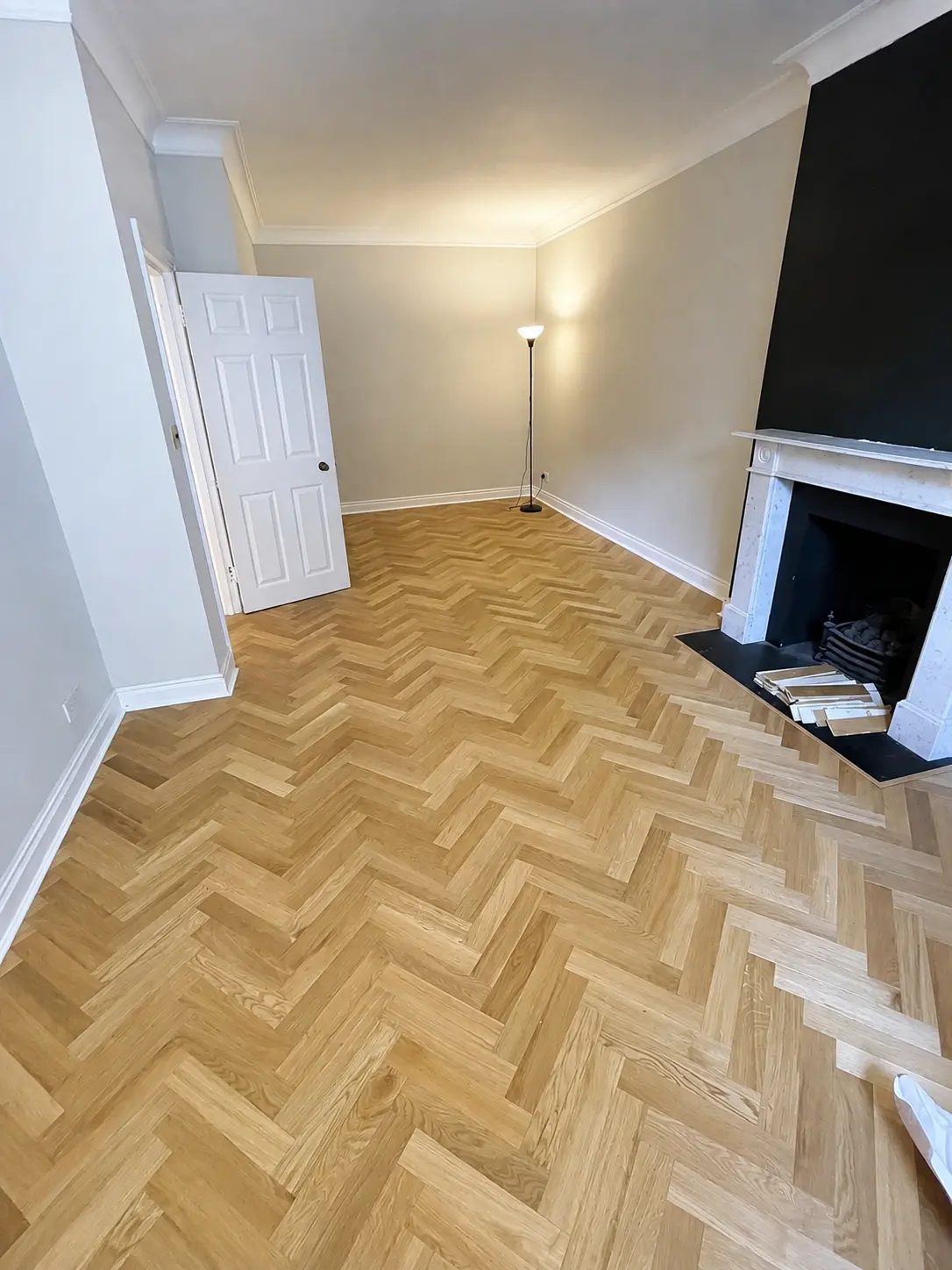 Light oak herringbone flooring with a white fireplace and black accent wall, Baker Street