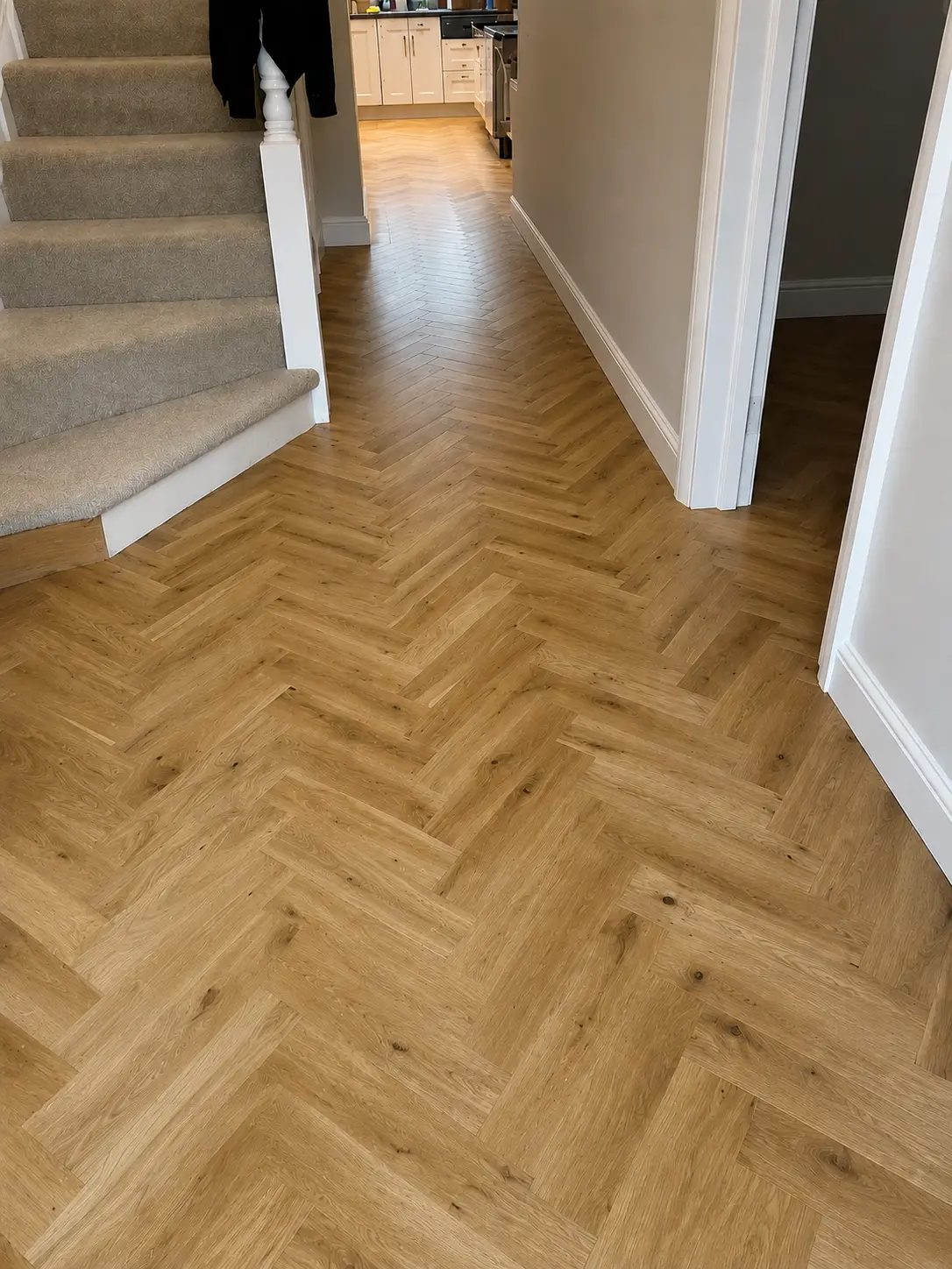 Light oak herringbone flooring in a hallway beside a staircase