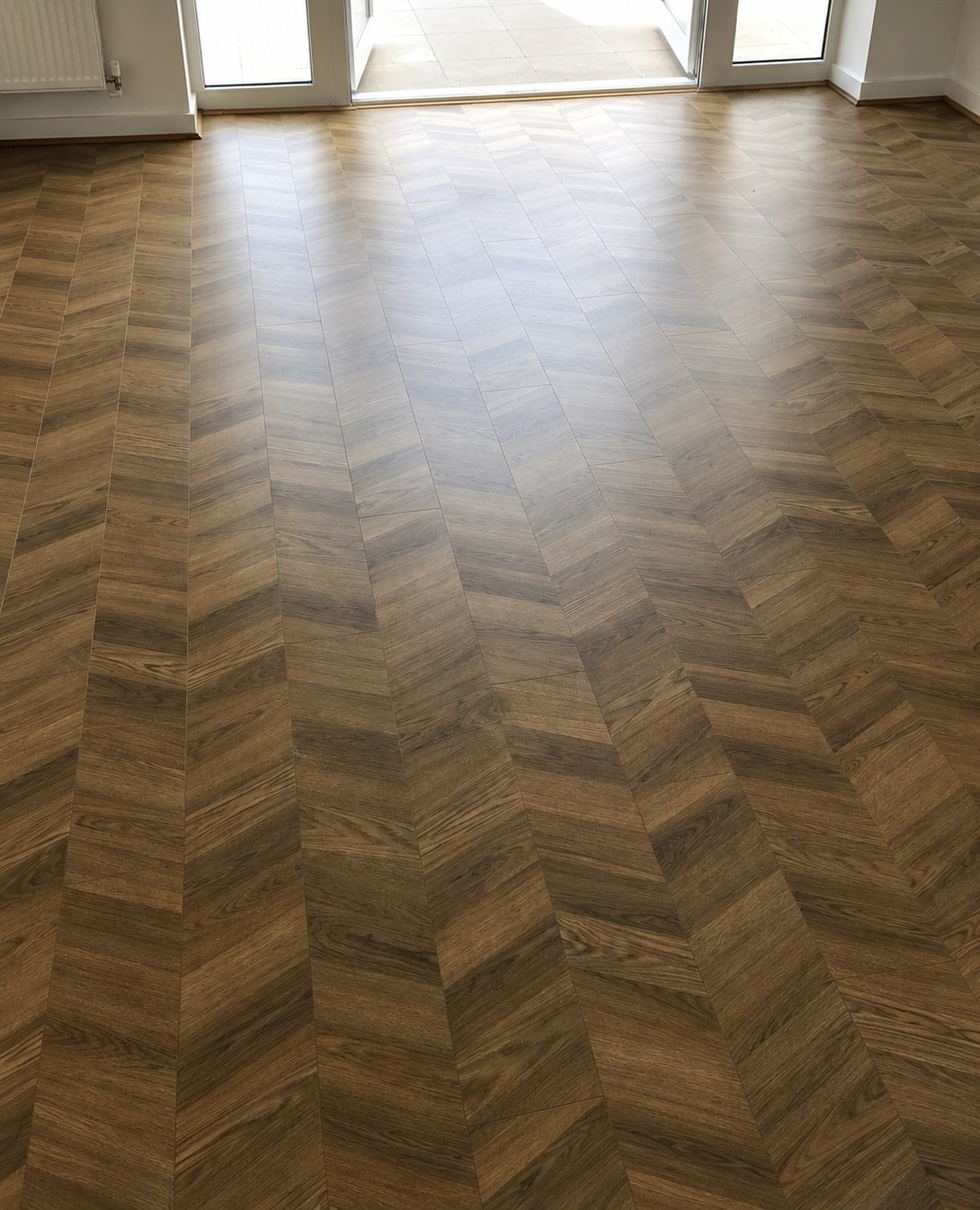 Chevron-pattern LVT flooring laid across a bright room with French doors