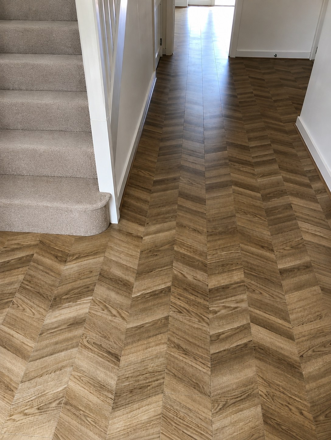 Chevron-style LVT flooring fitted in a hallway beside a carpeted staircase