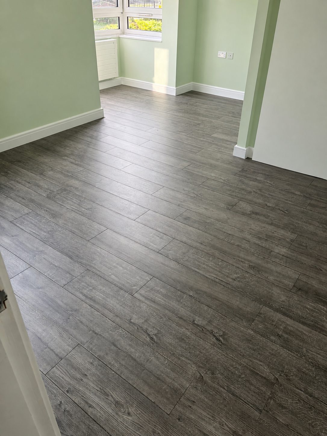 Grey wood-effect laminate flooring fitted through a through-lounge with sage green walls