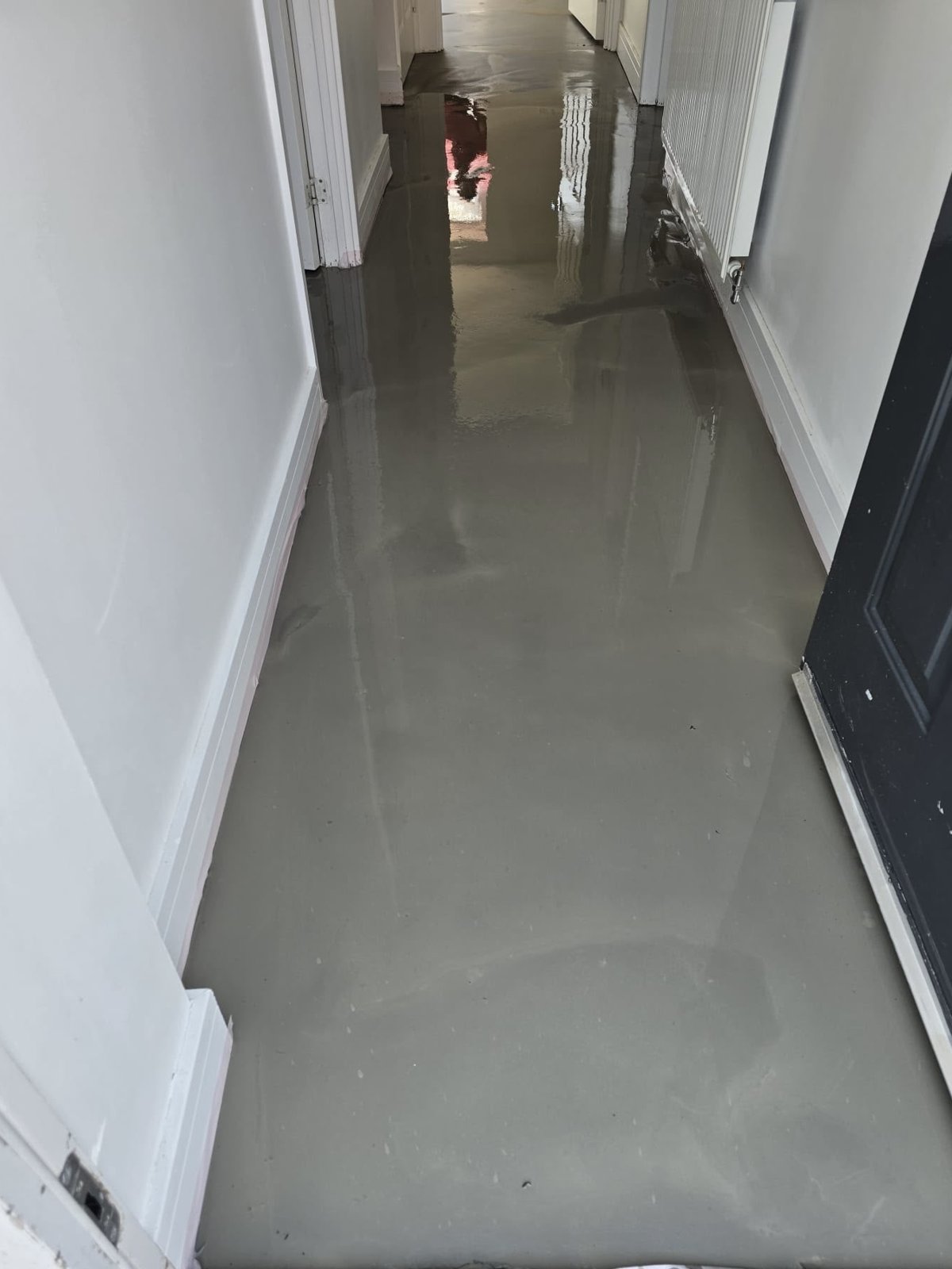 Freshly poured levelling compound drying across a hallway subfloor on a Pristine Flooring project
