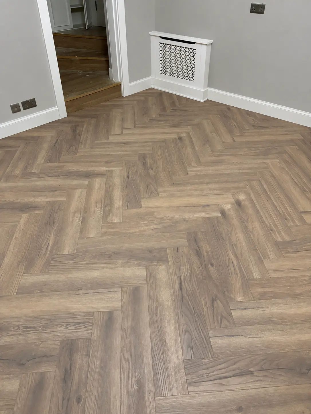 Rich brown herringbone flooring with white skirting boards