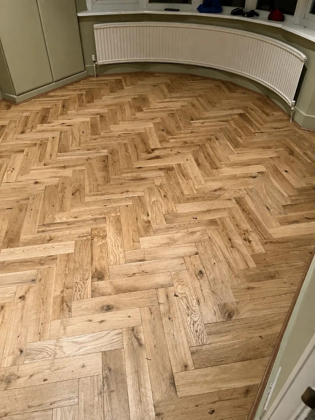 Light oak herringbone flooring fitted into a curved bay