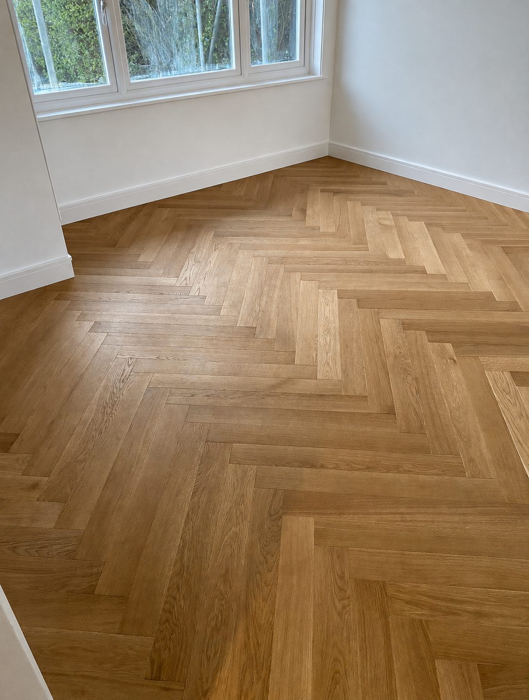Golden oak herringbone flooring laid in a bright bay-window room